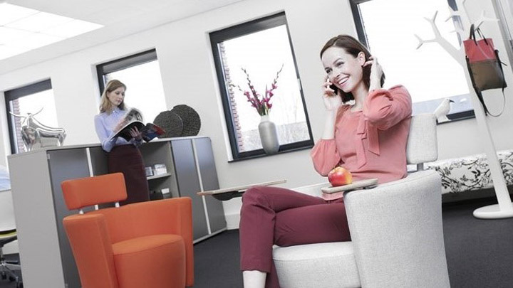 Mujer al teléfono en una sala equipada con la solución Soundlight Comfort. Iluminación de oficinas adaptada para hacer más confortable el lugar de trabajo.