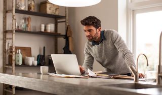 Hombre utilizando un laptop en una oficina doméstica bien iluminada con iluminación de tarea LED para una configuración eficiente del trabajo a distancia.